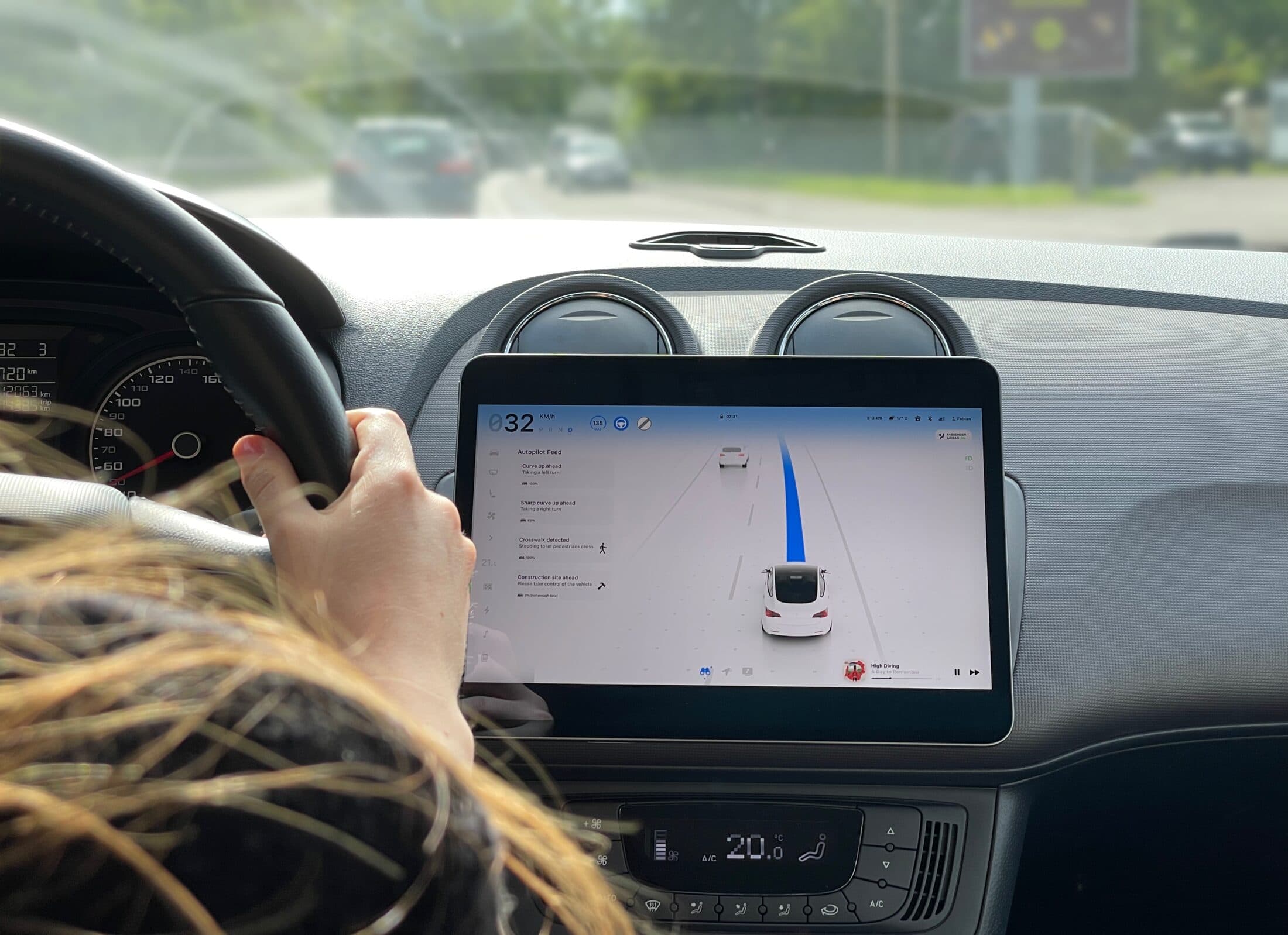 Two hands on a steering wheel in a real car, the Swift interface running on the centre screen with its blue autopilot path
